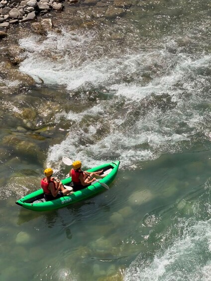 Two people kayaking on a river with clear water and rocks visible. 4