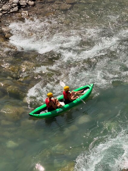 Two people kayaking on a river with clear water and rocks visible. 2