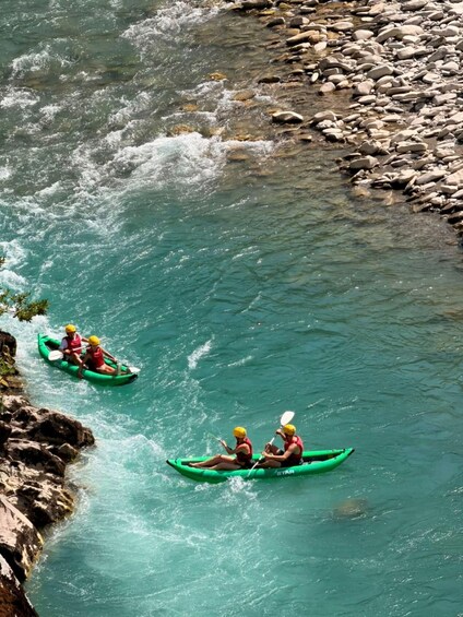 Two kayakers in green kayaks on a river with clear water and rocky banks. 5