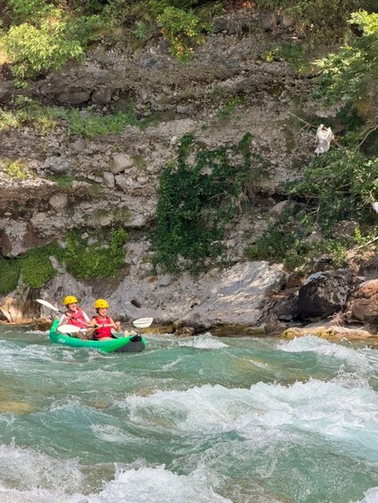 Two people kayaking on a river surrounded by rocky cliffs and greenery. 3