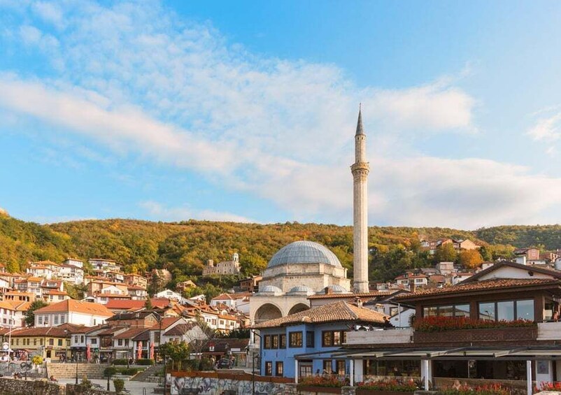 A town with a prominent minaret and a dome, surrounded by houses and a hilly landscape. 4