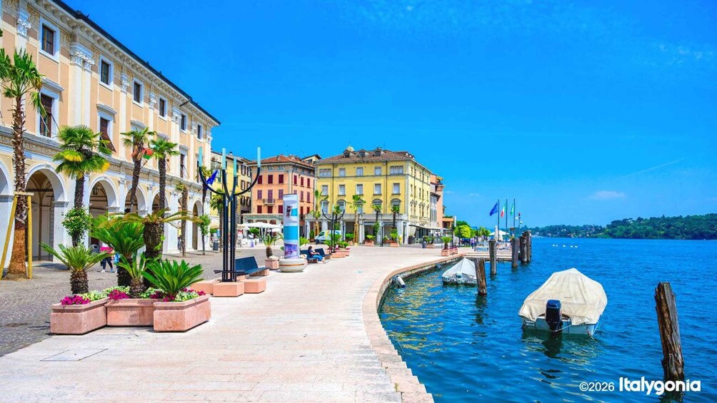A waterfront promenade with buildings, palm trees, and a clear blue sky. 2