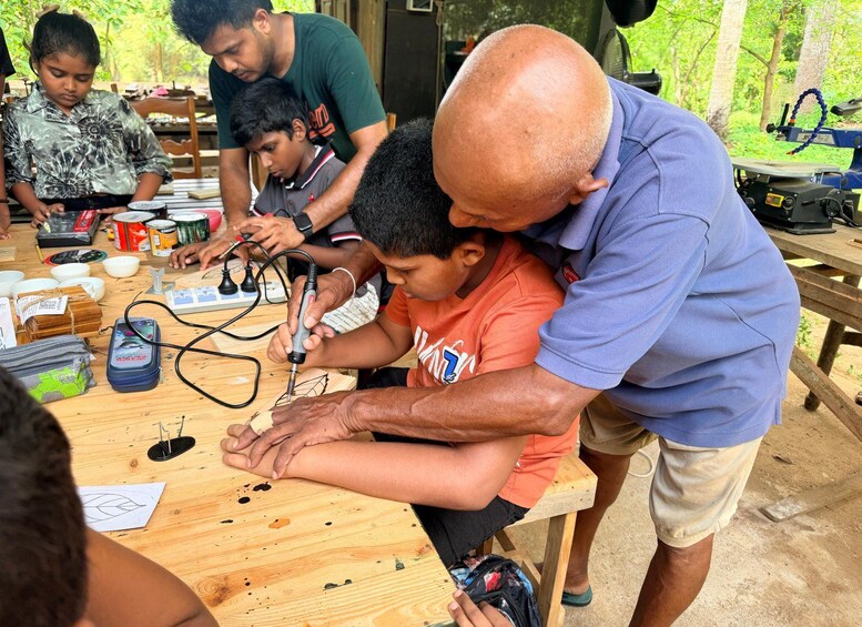 A group of people engaged in a woodworking activity, using tools and materials on a wooden table outdoors. 5