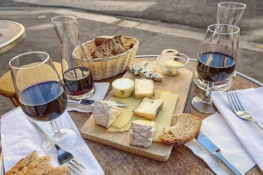 A cheese board with various cheeses, bread, and wine glasses on a wooden table. 2