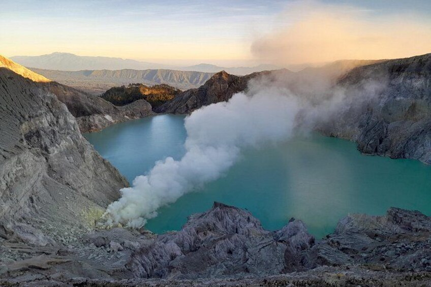 Un área geotérmica con un lago turquesa rodeado de terreno rocoso y vapor que se eleva del suelo. 4
