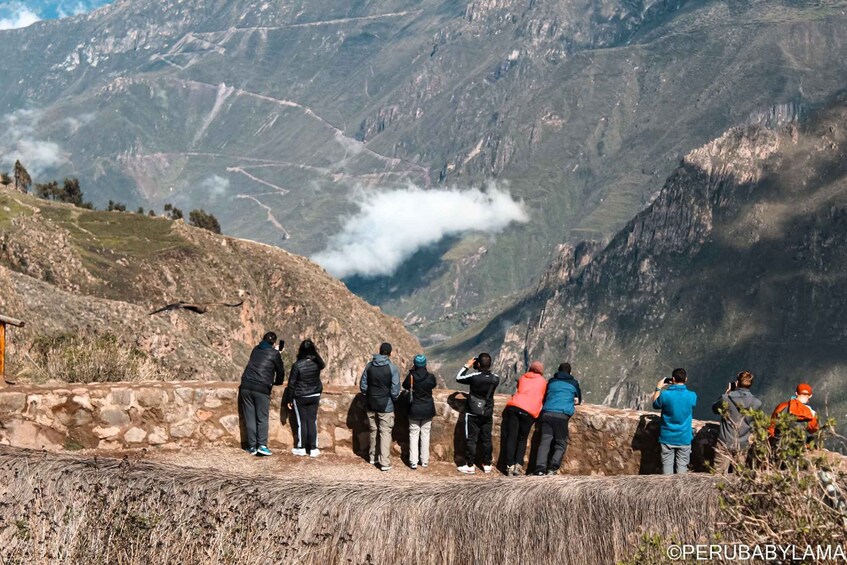 A group of people standing on a stone path overlooking a mountainous landscape with a visible cloud formation. 3