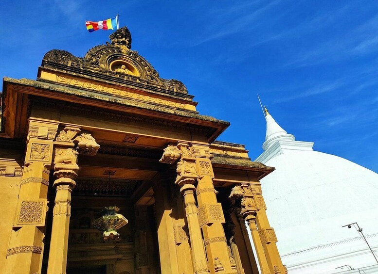 A temple entrance with ornate carvings and a white stupa in the background. 1