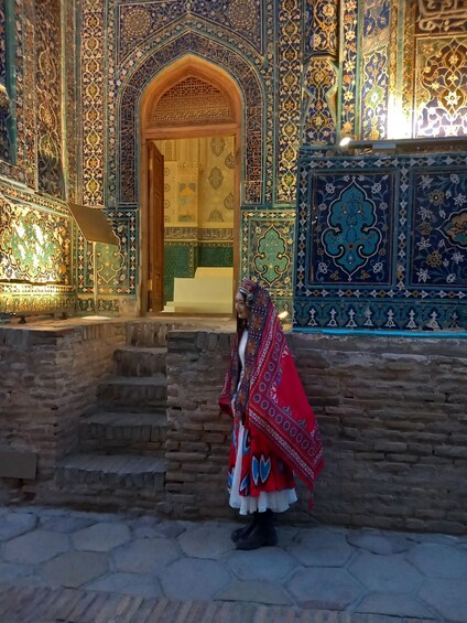 A person in traditional attire standing in front of a building with intricate tile work and an arched doorway. 5