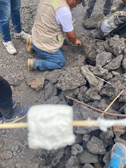 Una persona arrodillada sobre terreno rocoso, rodeada de otras, con una cuerda y un objeto blanco en primer plano. 4