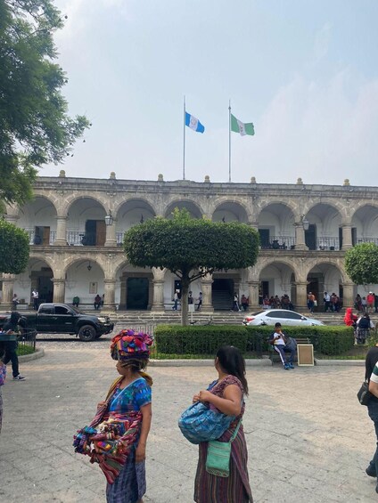 Un edificio histórico con arcos y banderas, un árbol y gente caminando. 5
