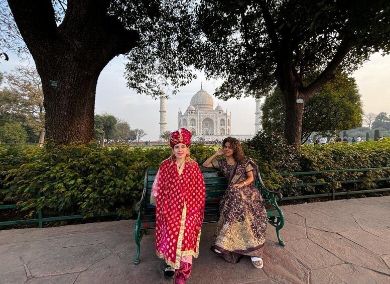 Two individuals seated on a bench with the Taj Mahal in the background. 2