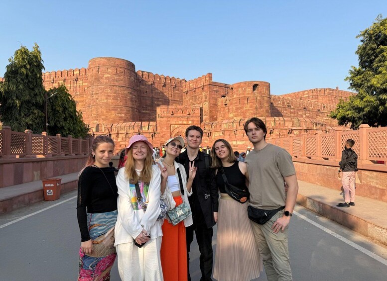 A group of people standing in front of a large, historic fort with red brick walls and intricate architecture. 4