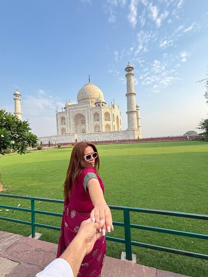 A person in a pink dress holding hands with someone else, standing in front of the Taj Mahal. 5