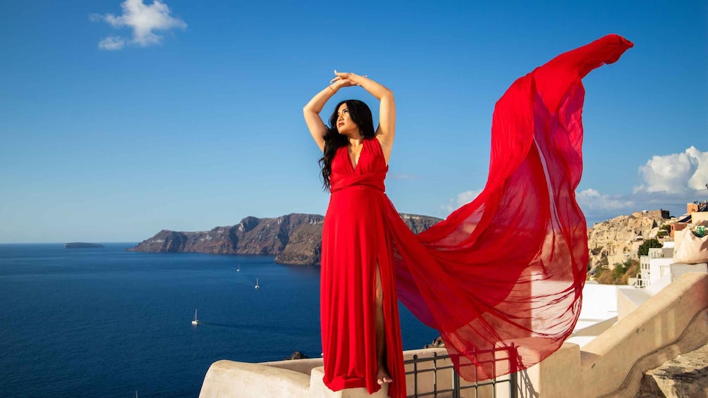 A woman in a red dress standing on a cliff overlooking the sea with boats in the distance. 5