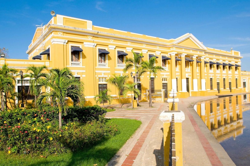 A yellow building with columns and a reflection in the water. 1