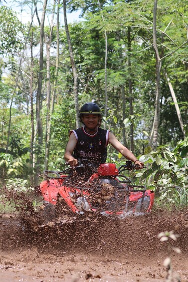 Una persona guida un quad rosso lungo un sentiero fangoso in una zona boschiva. 3