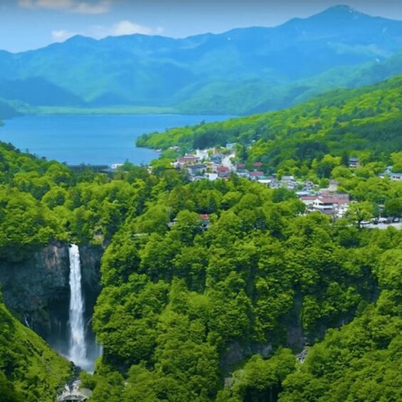 A lush green landscape with a waterfall, a lake, and a small settlement. 2