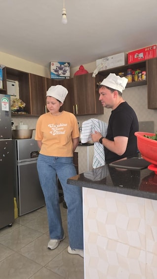 Two people in a kitchen, one wearing a chef's hat and the other in casual clothing. 5