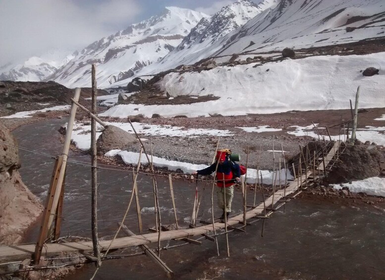 A person crossing a makeshift bridge over a river in a snowy mountainous area. 2
