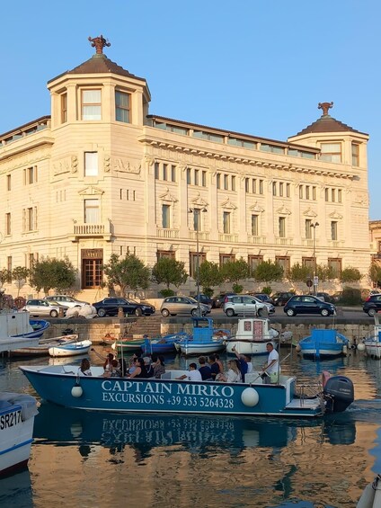 A large building with classical architecture, a marina with several boats, and parked cars along the waterfront. 3