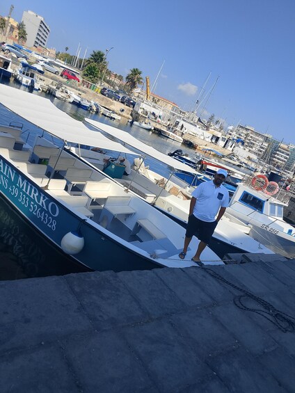 A marina with boats docked, a man standing on a boat, and buildings in the background. 1