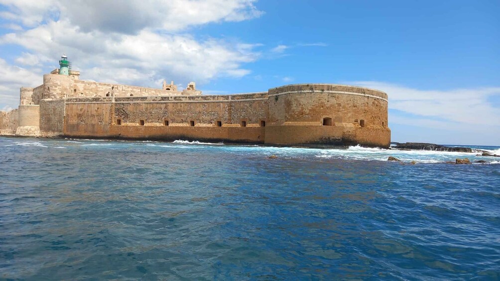 A coastal fortification with a lighthouse, waves crashing against the walls, and a clear sky. 4