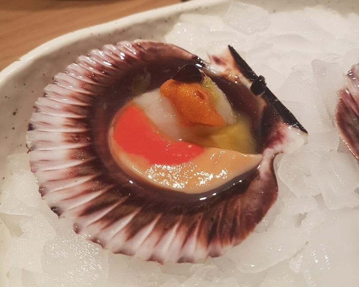 A scallop shell with a piece of orange and a slice of red vegetable on a bed of ice. 5