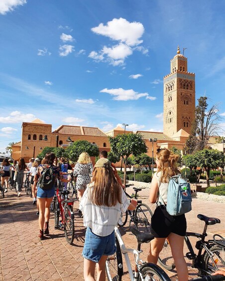 A group of people walking and cycling in a plaza with a tall tower in the background. 4