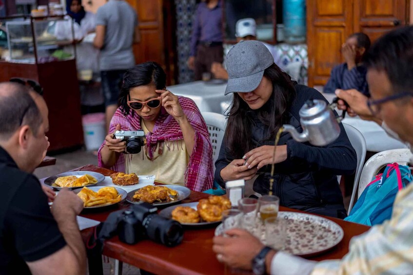 People sitting at a table with food and a teapot. 3