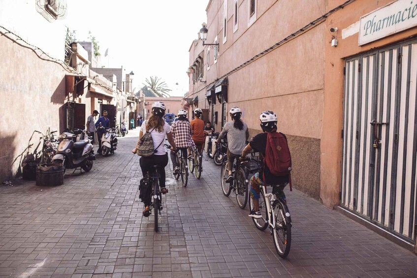A group of cyclists on a paved street lined with buildings and parked scooters. 2