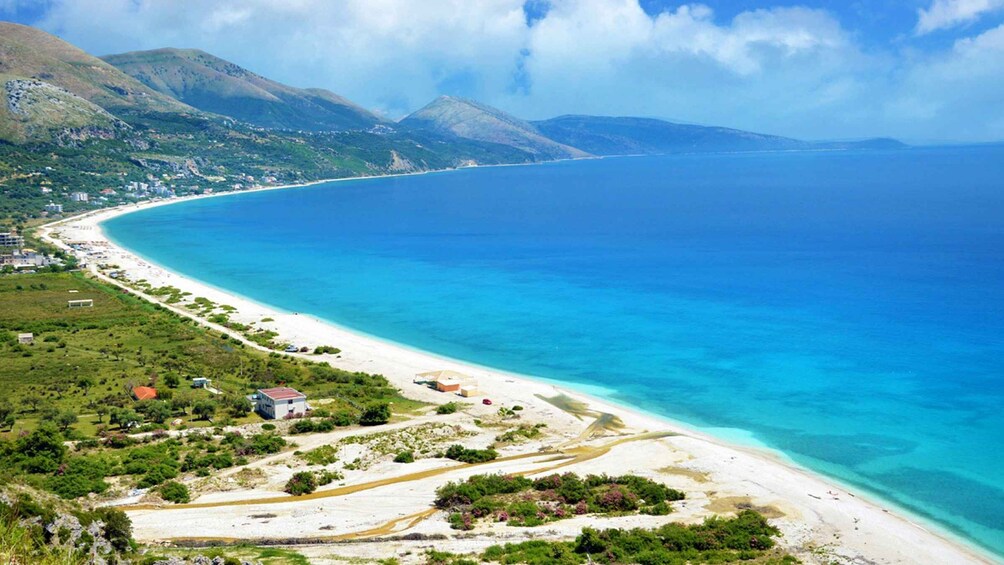 A coastal landscape with a sandy beach, clear blue waters, and green hills in the background. 1