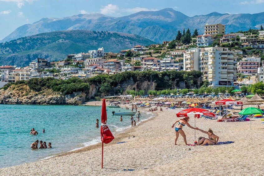 A beach with people swimming and sunbathing, umbrellas, and a mountainous backdrop. 4