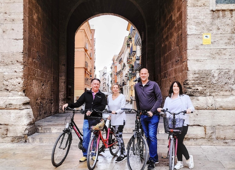 A group of people standing in front of a stone archway with bicycles. 1