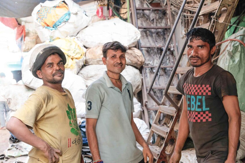 Three men standing in a cluttered storage area with sacks and wooden structures. 5