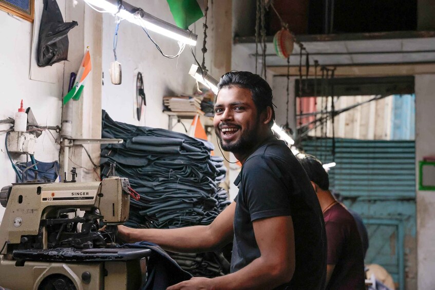 A person operating a Singer sewing machine in a workshop with stacks of fabric and sewing materials. 2