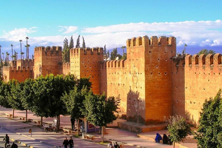 A historic fort with large stone walls and towers, surrounded by trees and a paved area with benches. 5