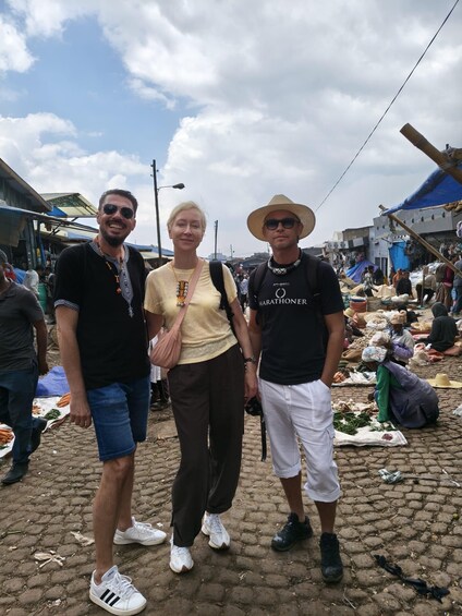 Three people standing in a market with vendors selling goods. 2