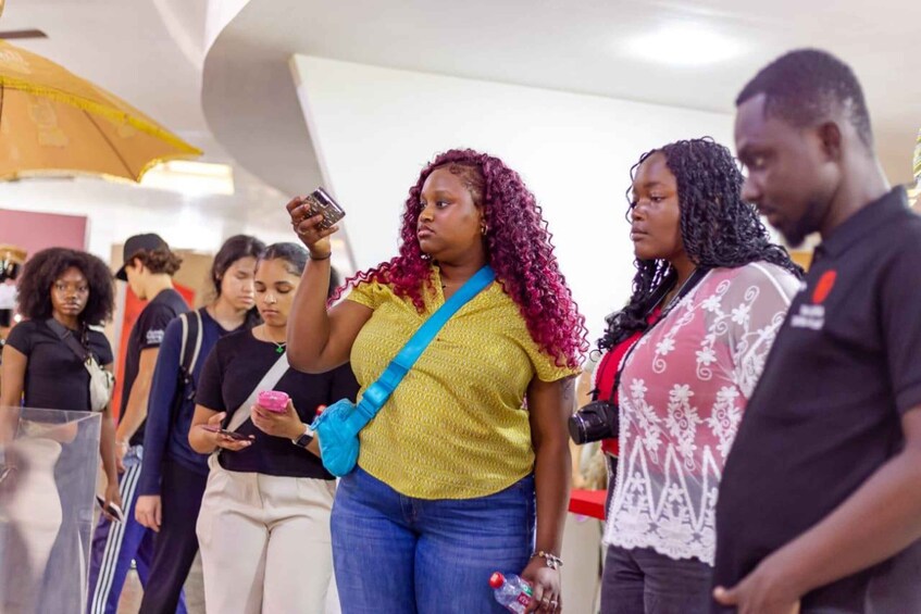 A group of people standing in a line, some holding phones and bags. 1