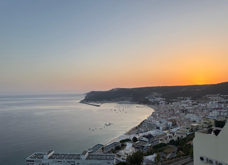 A coastal cityscape at sunset with a clear view of the sea, buildings, and a distant hill. 5
