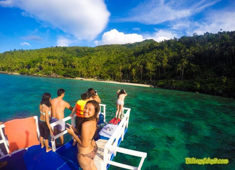 A group of people on a boat near a turquoise sea with a beach and dense forest in the background. 2