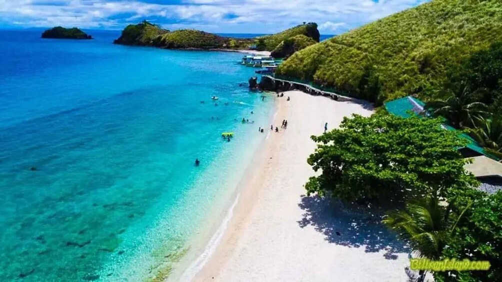 A beach with clear turquoise water, a sandy shore, and lush greenery. 1