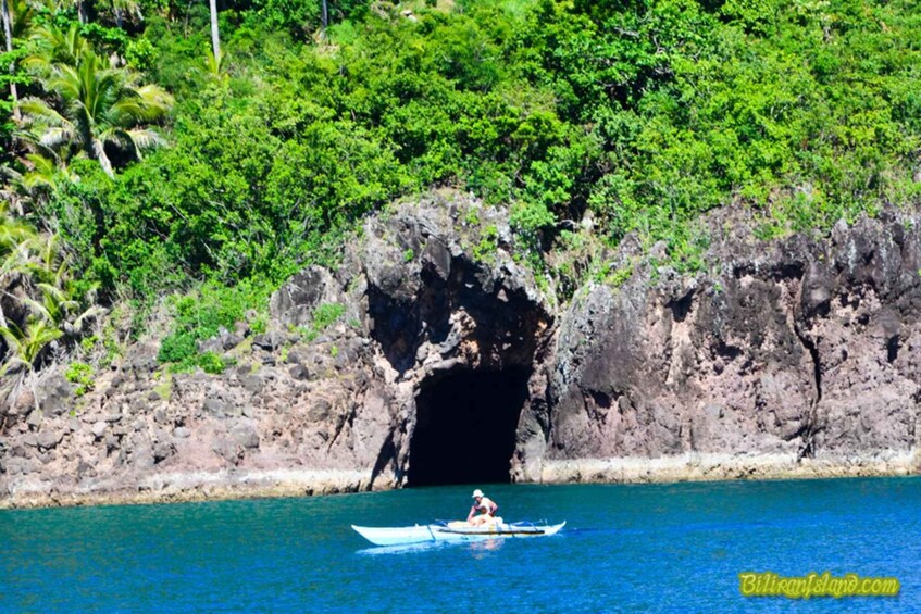A person kayaking near a rocky coastline with a cave entrance. 3