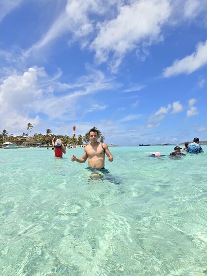 A person swimming in clear turquoise water with a lighthouse and palm trees in the background. 3