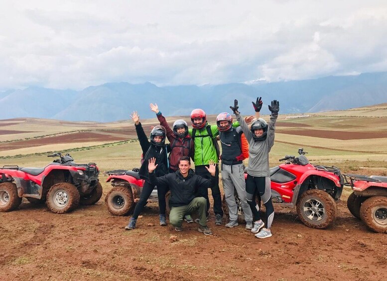 A group of people posing with red ATVs on a dirt road with a mountainous landscape in the background. 5