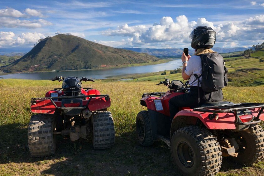 Two ATVs parked on a grassy field with a lake and mountains in the background. 1