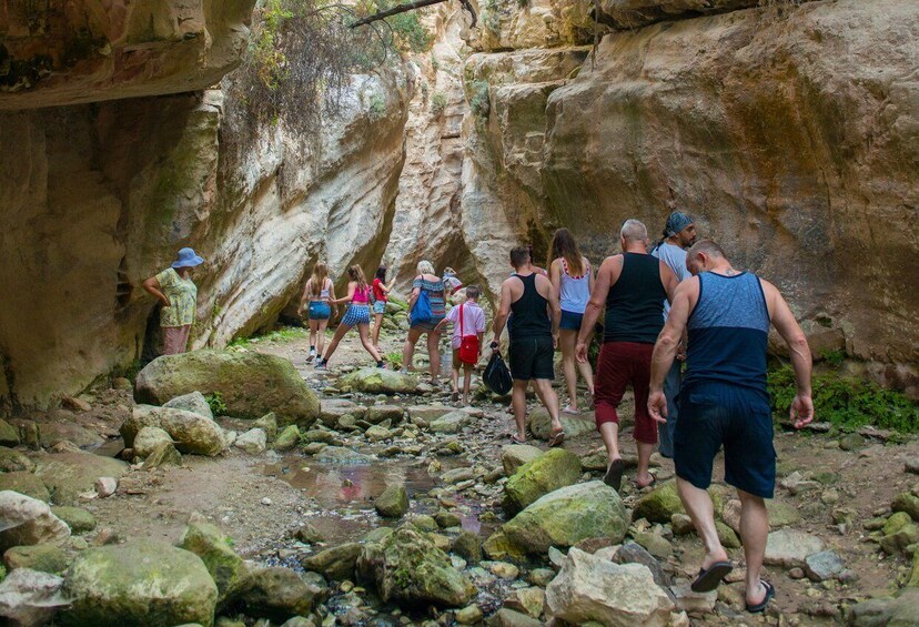A group of people hiking through a rocky canyon with large boulders and a narrow path. 3