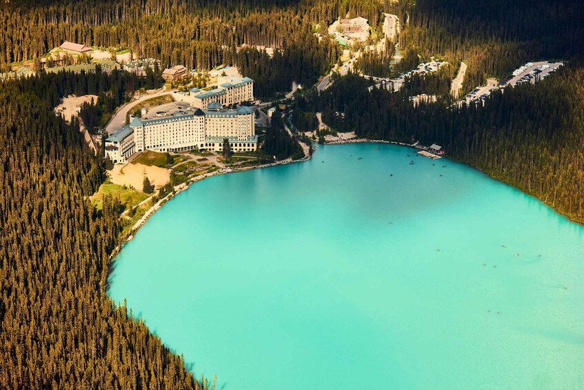 An aerial view of a resort with a large building and a turquoise lake surrounded by dense forest. 1