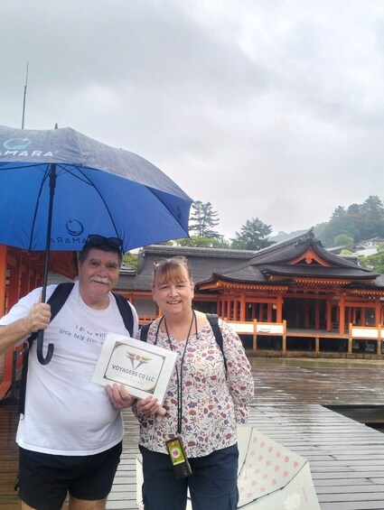 Two people standing on a wooden dock with a traditional building in the background. 4