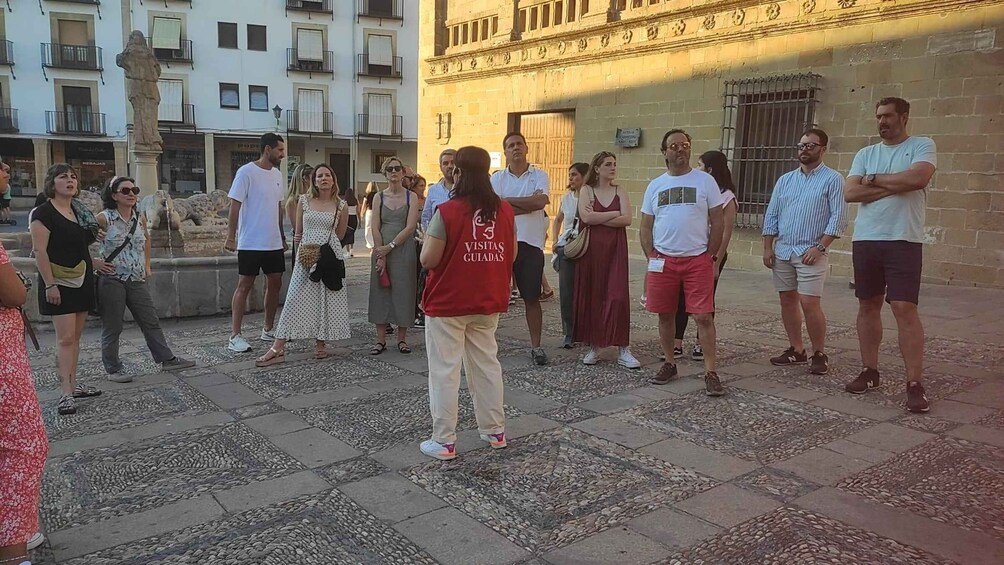 A group of people standing in a plaza with a stone floor and buildings in the background. 3
