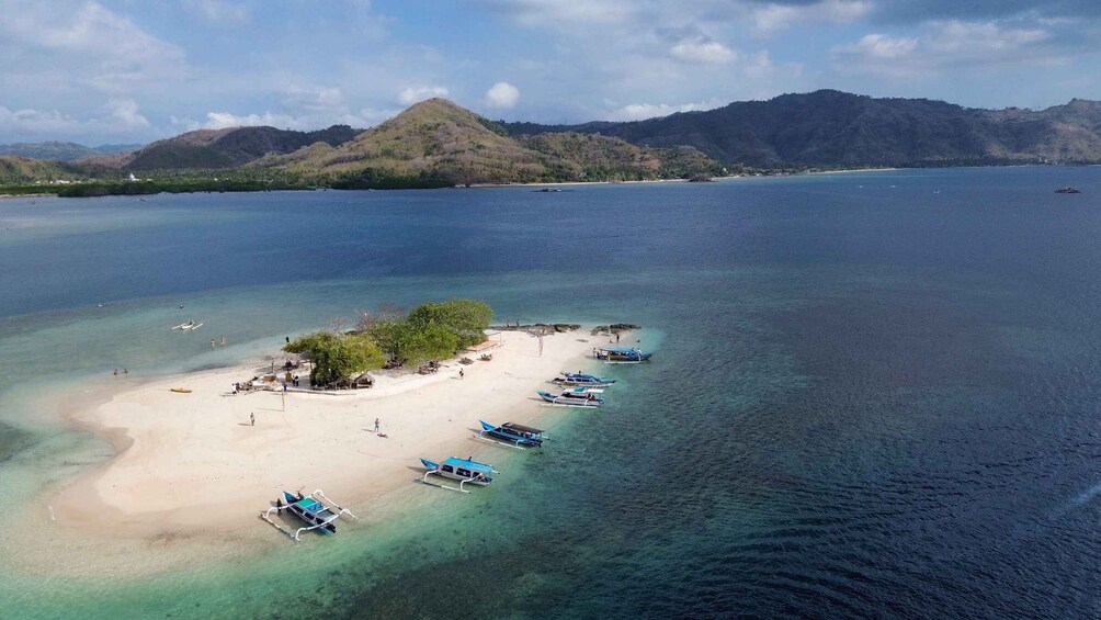 A tropical island with clear turquoise waters, a sandy beach, and several boats anchored near the shore. 2